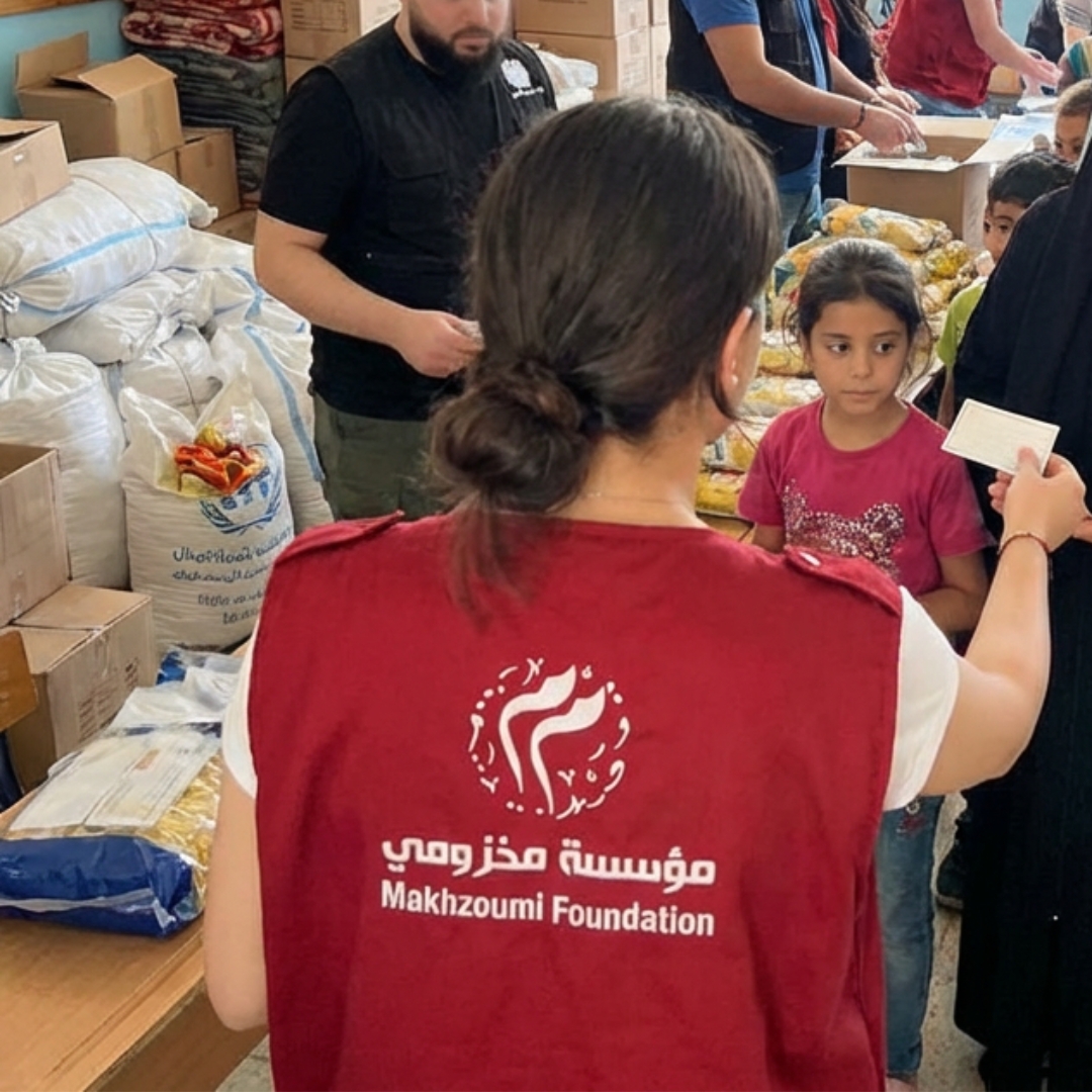 Volunteer wearing a Makhzoumi Foundation red vest distributes mattresses and relief supplies to displaced families inside a temporary shelter during the Lebanon emergency response.